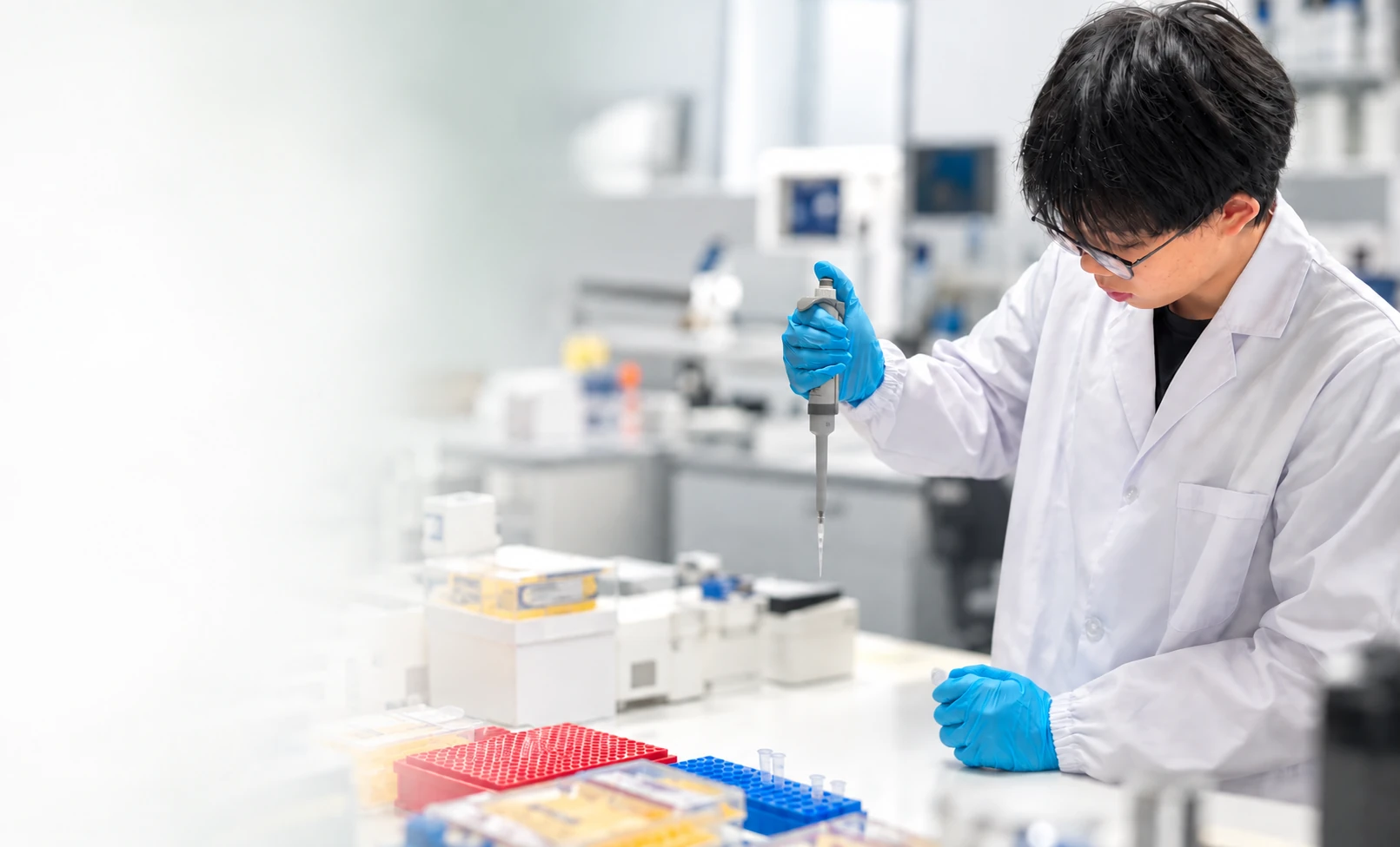 A student in a lab coat using a pipette at a laboratory bench